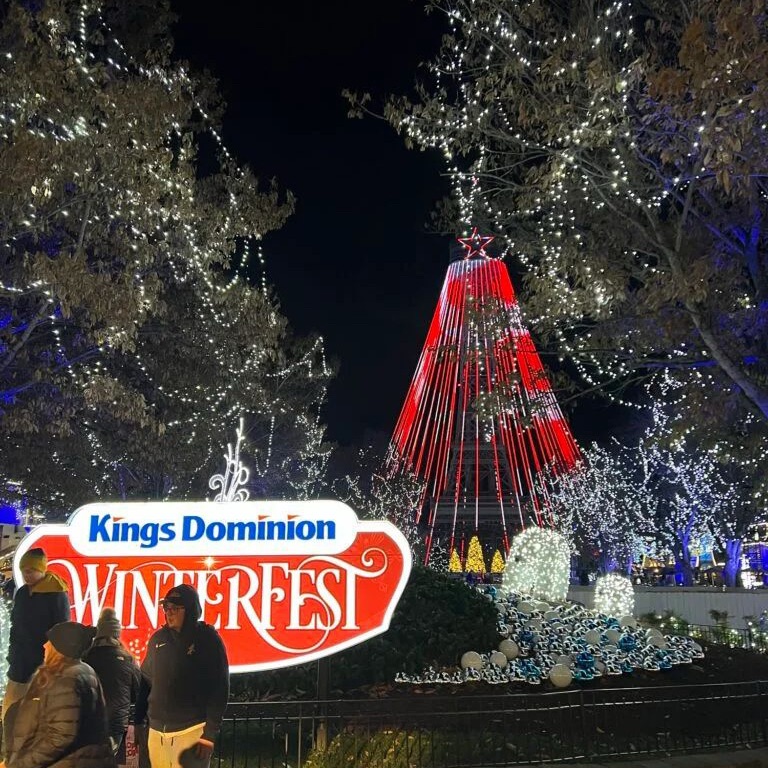 Illuminated holiday display featuring the 'Kings Dominion Winterfest' sign in front of the parks Eiffel Tower Replica adorned with lights, set in a festive atmosphere.